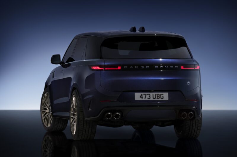Rear view of a dark blue Range Rover SUV with illuminated tail lights, quad exhaust pipes, and license plate "473 UBG" against a gradient blue background, celebrating the Range Rover Expands 2026 Sport Lineup with SV Black SV Carbon Editions.