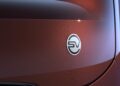 Close-up of an electric vehicle (EV) badge on a metallic brown car surface, highlighting the sleek, modern logo—echoing Range Rover’s expansion of its 2026 Sport lineup with SV Black SV Carbon and SV Bespoke Editions.