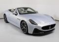 A silver Maserati convertible sports car, showcasing Italian luxury, is parked in a white studio with its top down, revealing a sleek black and white interior.