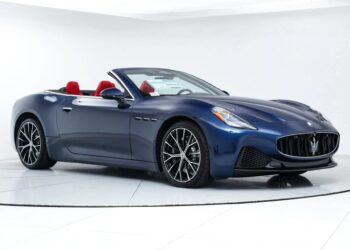 A blue Maserati convertible with red interior seats, this luxury car is displayed in a white showroom with a clear view of the front and side.