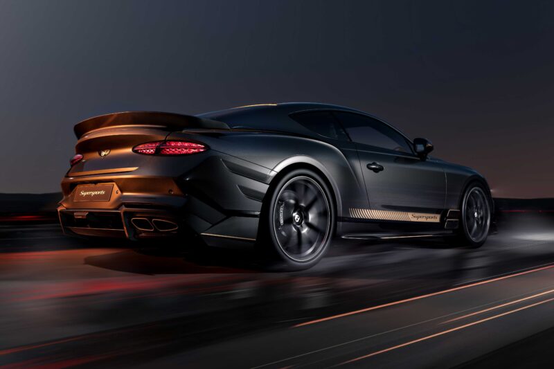 A matte black Bentley Supersports coupe speeds down a road at dusk, its illuminated taillights and "Supersports" branding highlighting the driver-focused design of this Continental GT.