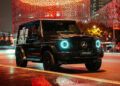 A black Mercedes-Benz G-Class Trophy Carrier SUV is parked on a city street at night, illuminated by red lights and a large panda graphic from League of Legends displayed on a building and reflected on the ground.