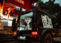 A shiny trophy sits in the open trunk of a black Mercedes-Benz G-Class SUV with “EARN YOUR LEGACY” on the side, parked near a traditional East Asian building with red pillars—a scene fit for League of Legends champions.