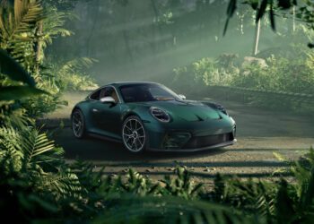 A stunning green Porsche Sonderwunsch 911 GT3 is parked on a dirt road, surrounded by dense, lush jungle vegetation with sunlight filtering through the trees.