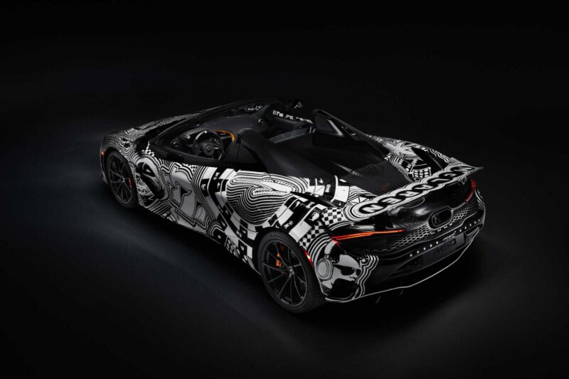 A black convertible sports car with a bold, abstract black and white camouflage pattern is parked in a dark studio—Project Viva Revealed: this one-of-one McLaren 750S Spider brings Las Vegas to life.