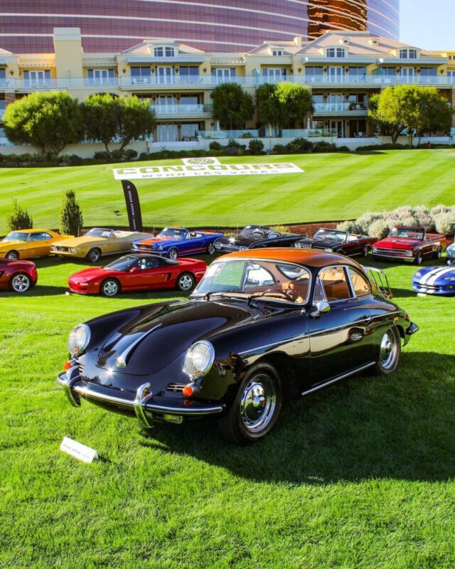 A classic black Porsche coupe is displayed on a grassy lawn with other vintage cars at the Broad Arrow Las Vegas Auction, set in front of a hotel or resort building on a sunny day.
