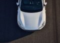 Aerial view of the front half of a white Polestar 4 parked on asphalt, showing the hood, headlights, and part of the windshield.