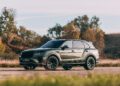 A metallic green luxury SUV, inspired by Bentley Honors Wartime Heroes with the Czech Squadron Collection and 2025 Remembrance Car, is parked outdoors on a paved surface, with grass and trees in the background under a clear sky.