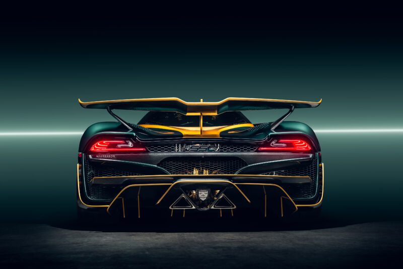 Rear view of the Tuatara Aggressor hypercar by SSC North America, featuring a prominent rear wing, illuminated taillights, and yellow accents against a dark gradient background.