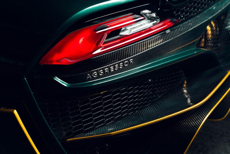 Close-up of a hypercar’s rear, featuring a red taillight, carbon fiber detailing, yellow accents, and the word “AGGRESSOR” engraved on the SSC North America Tuatara Aggressor’s body.