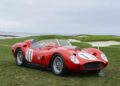 A vintage red sports car with the number 11 on its hood and doors is parked on grass near a golf course, capturing 75 years of automotive artistry against the backdrop of the sea and cloudy sky at Pebble Beach Concours d’Elegance.