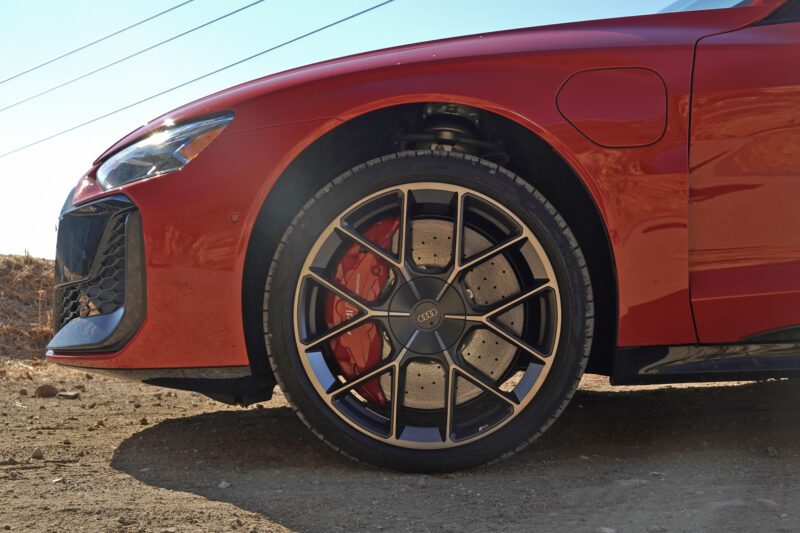 Close-up view of the front left wheel and fender of a red Audi, as featured in our review: 2025 Audi RS e-tron GT Performance. Showcases the wheel design, brake caliper, and part of the sculpted front bumper.