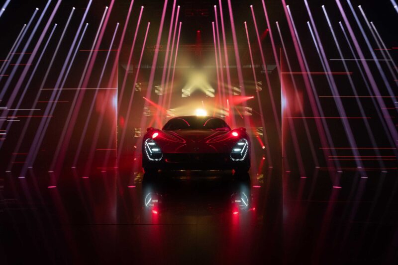 A red Alfa Romeo sports car is illuminated by dramatic red and white lights in a dark, futuristic setting with reflective floors, capturing the excitement of a Maserati launch and the style of BOTTEGAFUORISERIE.