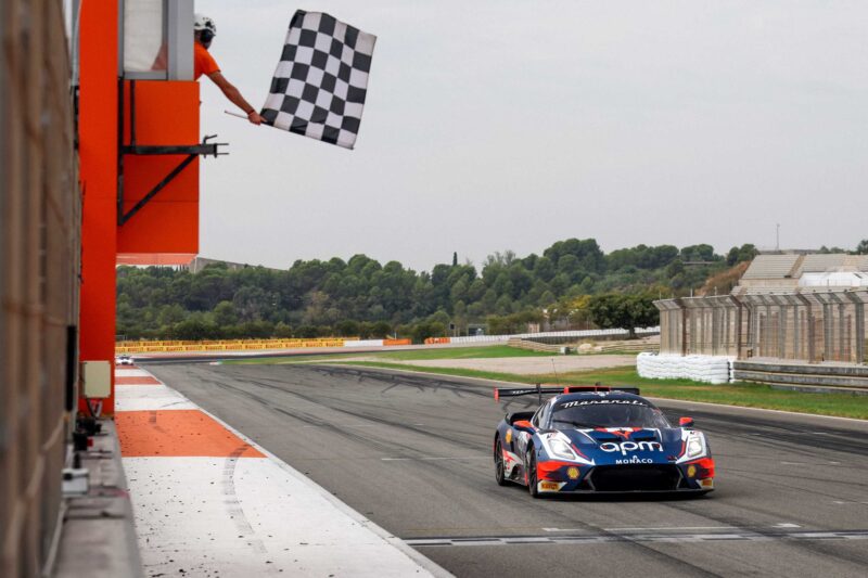 An Alfa Romeo Maserati races across the finish line on the track as an official waves a checkered flag from a platform above, celebrating the BOTTEGAFUORISERIE launch.