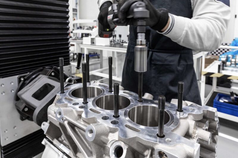 A person in gloves uses a power tool to assemble or work on an Alfa Romeo engine block in a clean, BOTTEGAFUORISERIE industrial workshop setting.