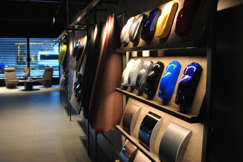 Wall display featuring various car paint color samples and BOTTEGAFUORISERIE material swatches in a modern showroom, with chairs and a table visible in the background—perfect for exploring Alfa Romeo Maserati Launch options.