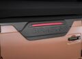 Close-up of a vehicle's rear section with a carbon fiber panel, embossed "BRABUS" logo, and a horizontal red brake light on its beige exterior—showcasing details inspired by the Brabus Debuts 800 Cabrio and XL 800 Cabrio.