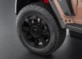 Close-up view of a black alloy wheel and tire on a beige SUV, showcasing the detailed tread pattern and red brake caliper—an attention to detail seen in models like the Brabus Debuts 800 Cabrio and XL 800 Cabrio.