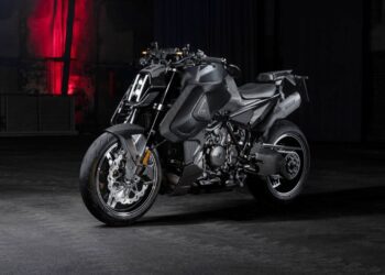 A matte black BRABUS 1400 R Signature Edition sport motorcycle is parked indoors on a concrete floor, with a dim background and red light illuminating the wall behind it, hinting at its exclusive 2026 allure.