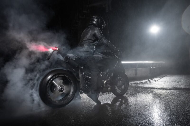 A motorcyclist in black gear performs a burnout on a wet road at night astride the BRABUS 1400 R Signature Edition, with smoke billowing from the rear tire and a bright light illuminating the dramatic 2026 scene.