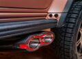 Close-up of a car's dual exhaust pipes with red accents, carbon fiber trim, and part of a rugged tire visible—capturing the bold styling featured as Brabus debuts 800 Cabrio and XL 800 Cabrio models.