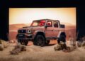 A customized pink Brabus 4x4 SUV with red interior is parked on sand with rocks and dry plants, against a desert backdrop and sunset lighting—channeling the bold spirit seen when Brabus debuts 800 Cabrio and XL 800 Cabrio models.