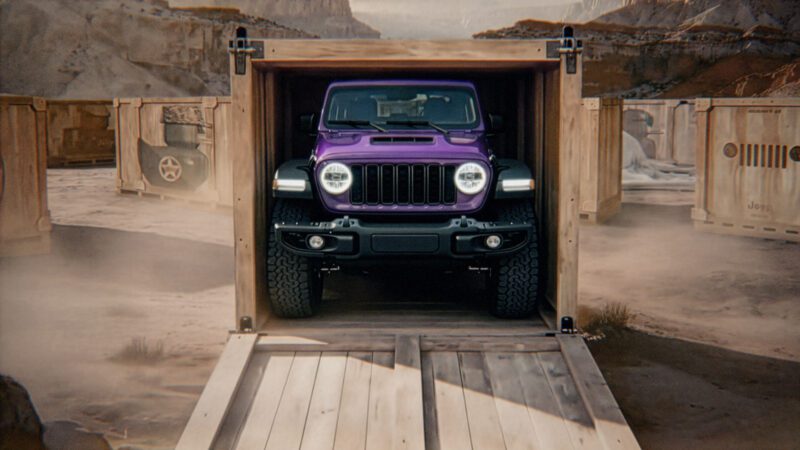 A purple Jeep Moab 392, part of Jeep’s 85th Anniversary Limited Edition Series, is parked inside an open wooden shipping crate in a desert setting, with other crates visible in the background.