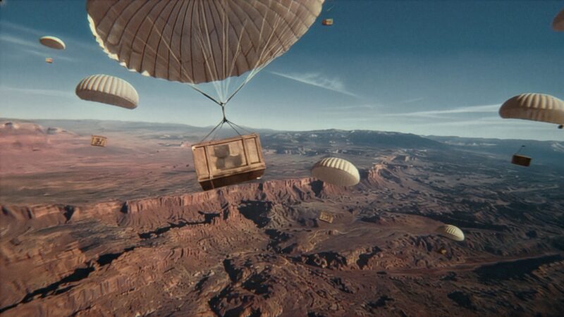 Several large crates attached to parachutes descend over a vast desert canyon landscape under a clear blue sky, echoing the adventurous spirit of Jeep's 85th Anniversary Limited Edition Series with the Moab 392.