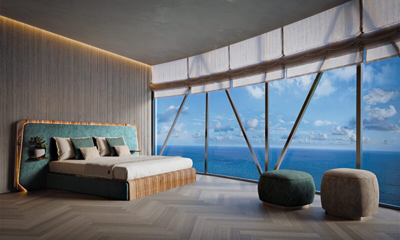 Modern bedroom in Bentley Residences with floor-to-ceiling windows offering an ocean view, a bed with a blue headboard, and two round ottomans on a herringbone wood floor—true Miami penthouses luxury real estate.