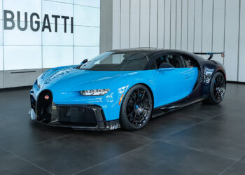 A blue and black Bugatti Chiron Pur Sport in striking French Racing Blue is on display in a modern showroom with large “BUGATTI” signage in the background, ready and available for sale.