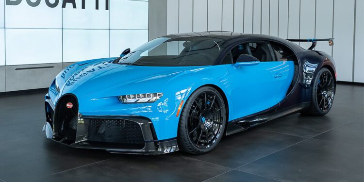 A blue and black Bugatti Chiron Pur Sport in striking French Racing Blue is on display in a modern showroom with large “BUGATTI” signage in the background, ready and available for sale.