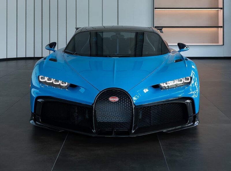 A bright blue Bugatti Chiron Pur Sport is parked indoors, photographed from the front, showcasing its sleek design and distinctive grille—now available for sale.