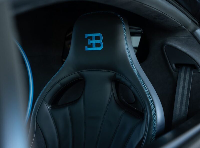 Close-up of a black Bugatti Chiron Pur Sport car seat with blue stitching and the Bugatti logo embroidered in blue on the headrest. For sale.