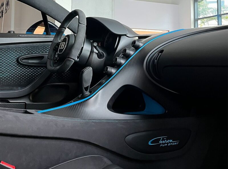 Interior view of a Bugatti Chiron Pur Sport for sale, featuring French Racing Blue accents on the steering wheel, dashboard, and door, highlighting its sporty trim and luxurious design.
