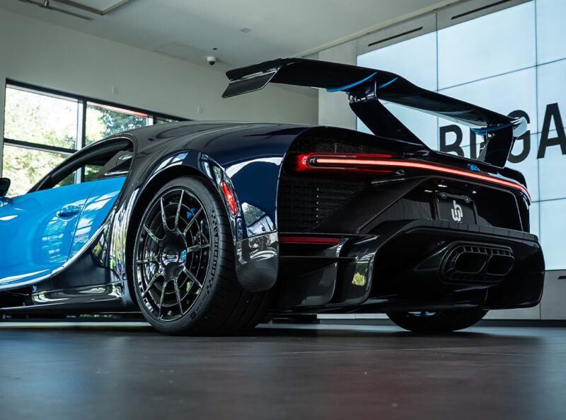 A 2021 Bugatti Chiron Pur Sport in French Racing Blue and black is parked indoors, showcasing its rear end, prominent spoiler, and intricate wheel design.