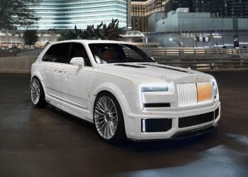 A white luxury SUV with custom wheels and an illuminated grille is parked on a city street at night, showcasing Urban Automotive style against the backdrop of modern buildings.