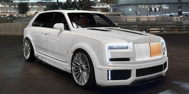 A white luxury SUV with custom wheels and an illuminated grille is parked on a city street at night, showcasing Urban Automotive style against the backdrop of modern buildings.