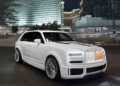 A white Custom Cullinan luxury SUV with bespoke modifications is parked on a city street at night, framed by modern high-rise buildings in the background.