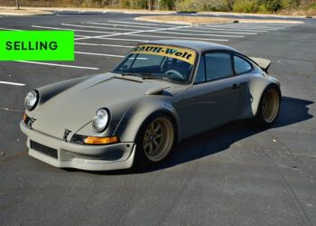 A matte grey modified Porsche 911 RSR with wide fenders and gold wheels is parked in an empty lot; a green "SELLING" banner appears in the top left corner, evoking the excitement of car auctions.