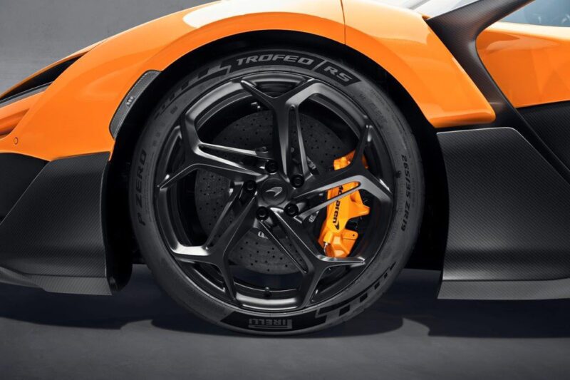 Close-up of a black alloy wheel and tire with visible brake disc and orange caliper on an orange sports car.