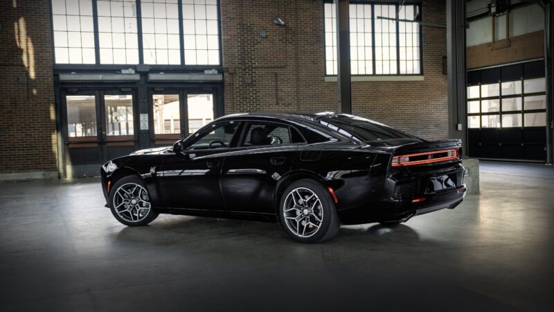 A powerful sedan with modern muscle styling is parked inside an industrial-style garage, surrounded by large windows and brick walls.