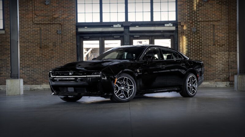 A black Dodge Charger electric car, known as a powerful sedan and among the best sedan options, is parked inside an industrial-style building with brick walls and large windows.