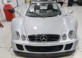 A silver Mercedes-Benz CLK-GTR Roadster convertible sports car, valued as a $13M car, is parked indoors on a clean, white floor with its top down and front view visible.