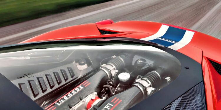Close-up view of the last naturally aspirated mid-engine V8 Ferrari ever built, its powerful engine visible through a transparent cover, with part of the red car and road in the background.