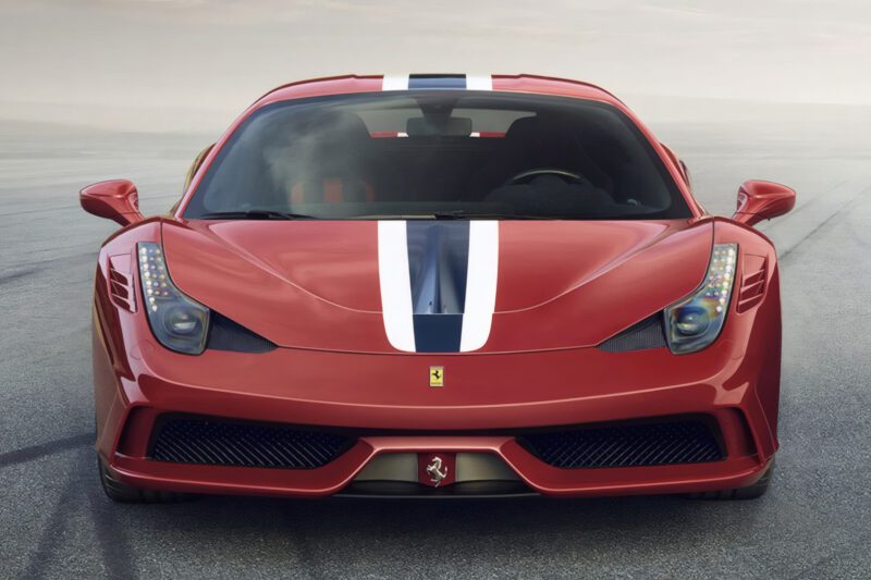A red Ferrari sports car with a white and blue racing stripe—the last naturally aspirated mid-engine V8 Ferrari ever built—is parked on pavement, viewed from the front.