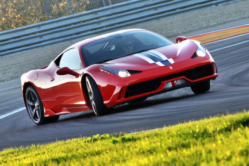 A red Ferrari sports car with white racing stripes, known as the last naturally aspirated mid-engine V8 Ferrari ever built, drives on a racetrack, taking a corner at speed.