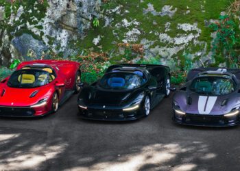 Three sports cars—one red, one black, and an ultra-rare Ferrari Daytona SP3 with white stripes—are parked side by side on a paved area next to a mossy rock wall, possibly showcased by Miller Motorcars.