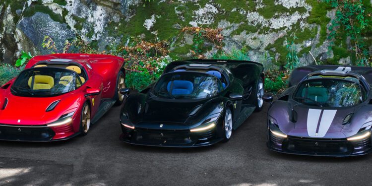 Three sports cars—one red, one black, and an ultra-rare Ferrari Daytona SP3 with white stripes—are parked side by side on a paved area next to a mossy rock wall, possibly showcased by Miller Motorcars.