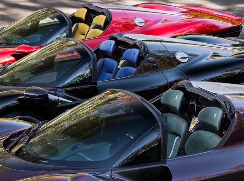 Four ultra-rare convertible sports cars, including a Ferrari Daytona SP3, are parked closely together at Miller Motorcars, showcasing sleek exteriors in black, red, and maroon and vibrant interiors in blue, yellow, and green.