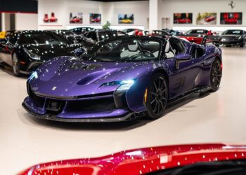 A Violetto Dino Ferrari SF90 Spider is displayed at Ferrari Lake Forest's luxury showroom, surrounded by other high-end vehicles under bright lighting.